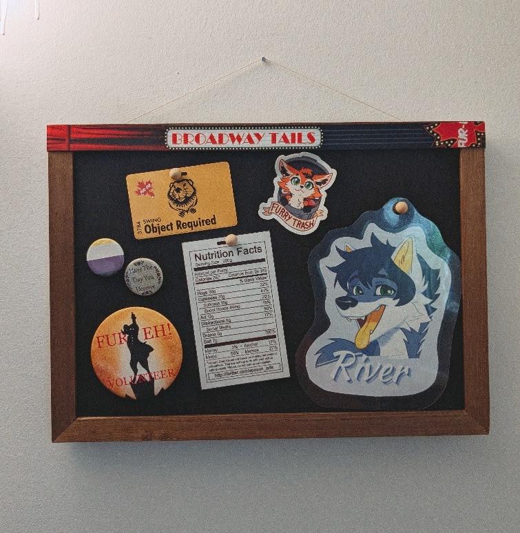 A cork board filled with souvenirs from Fur-Eh Broadway Tails, as the lanyard on top of it reads. There's a bunch of pins, "Furry Trash" sticker with a fox proudly peeking out of a rubbish bin, a blue fox fursona badge, and Furry Nutrition Facts sheet by Apoxon